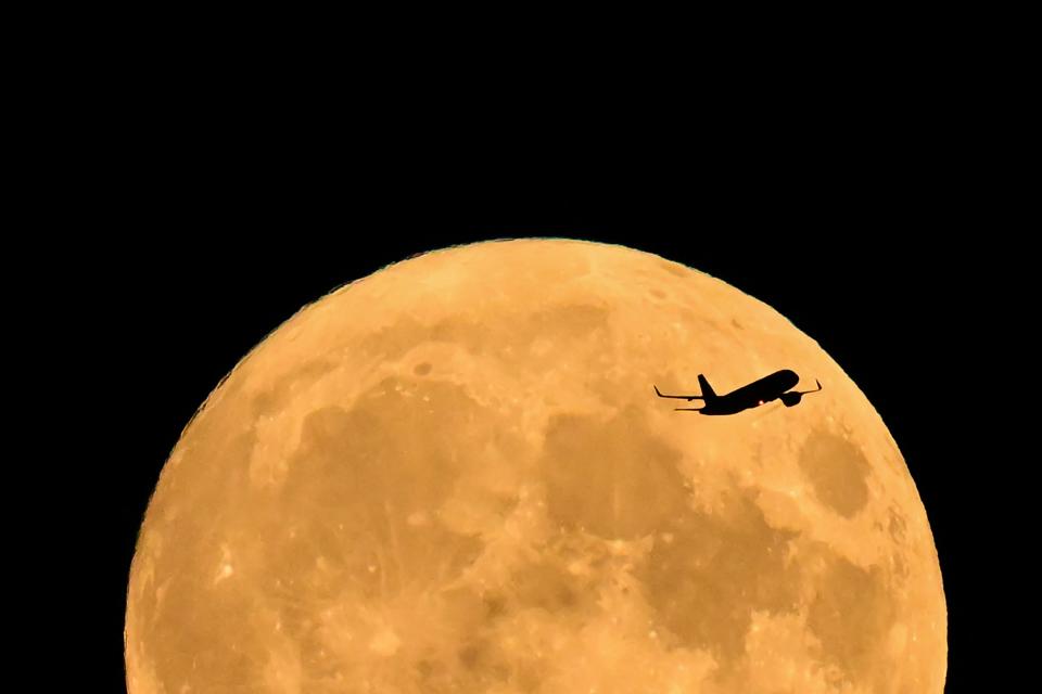 A British Airways Airbus A320 from Barcelona heading to Heathrow Airport flies past the full moon rising in London on Aug. 30, 2023.