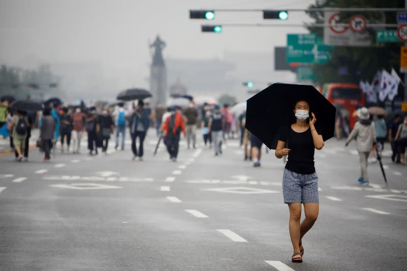 A woman wearing a mask walks past members of conservative civic groups who take part in an anti-government protest, as concerns over a fresh wave of the coronavirus disease (COVID-19) cases grow, in central Seoul