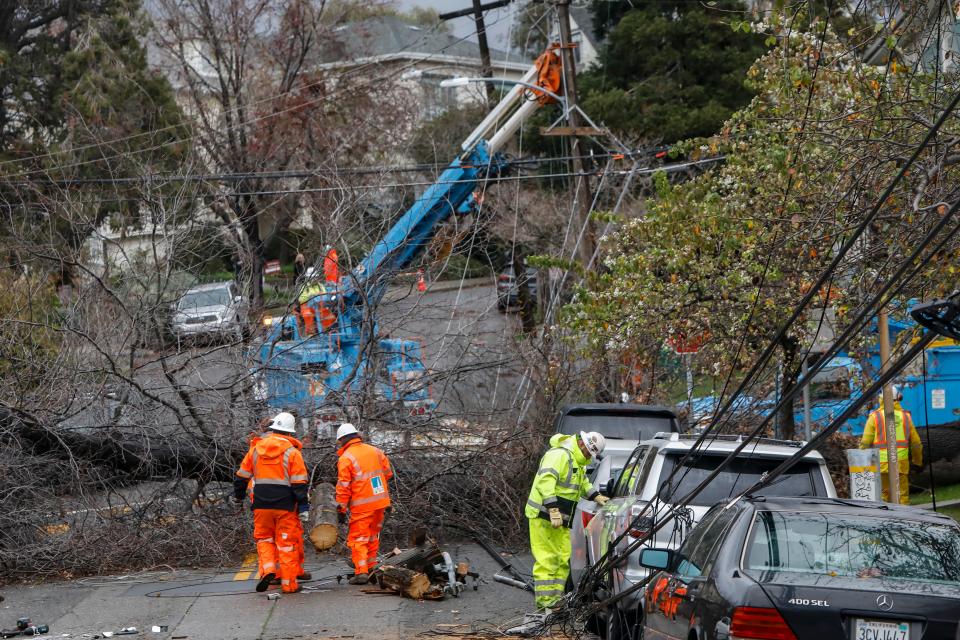 PG&E utility workers clear a fallen tree that took down some power lines next to Bella Vista Elementary School in the Bella Vista neighborhood in Oakland, Calif., on Wednesday, Jan. 4, 2023.