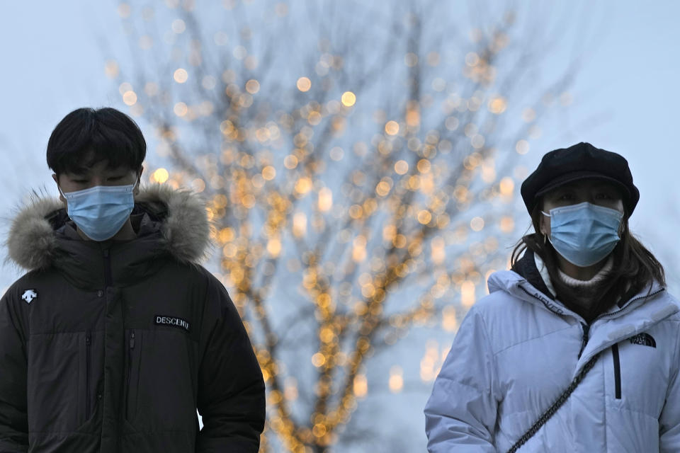 Residents wearing masks to protect from the coronavirus walks near decorative lights on a tree in Beijing, China, Thursday, Jan. 20, 2022. The sweeping "zero-tolerance" policies that China has employed to protect its people and economy from COVID-19 may, paradoxically, make it harder for the country to exit the pandemic. (AP Photo/Ng Han Guan)