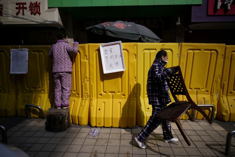 A resident pays for groceries by standing on a tree stump to peer over barriers set up to ring fence a wet market on a street in Wuhan