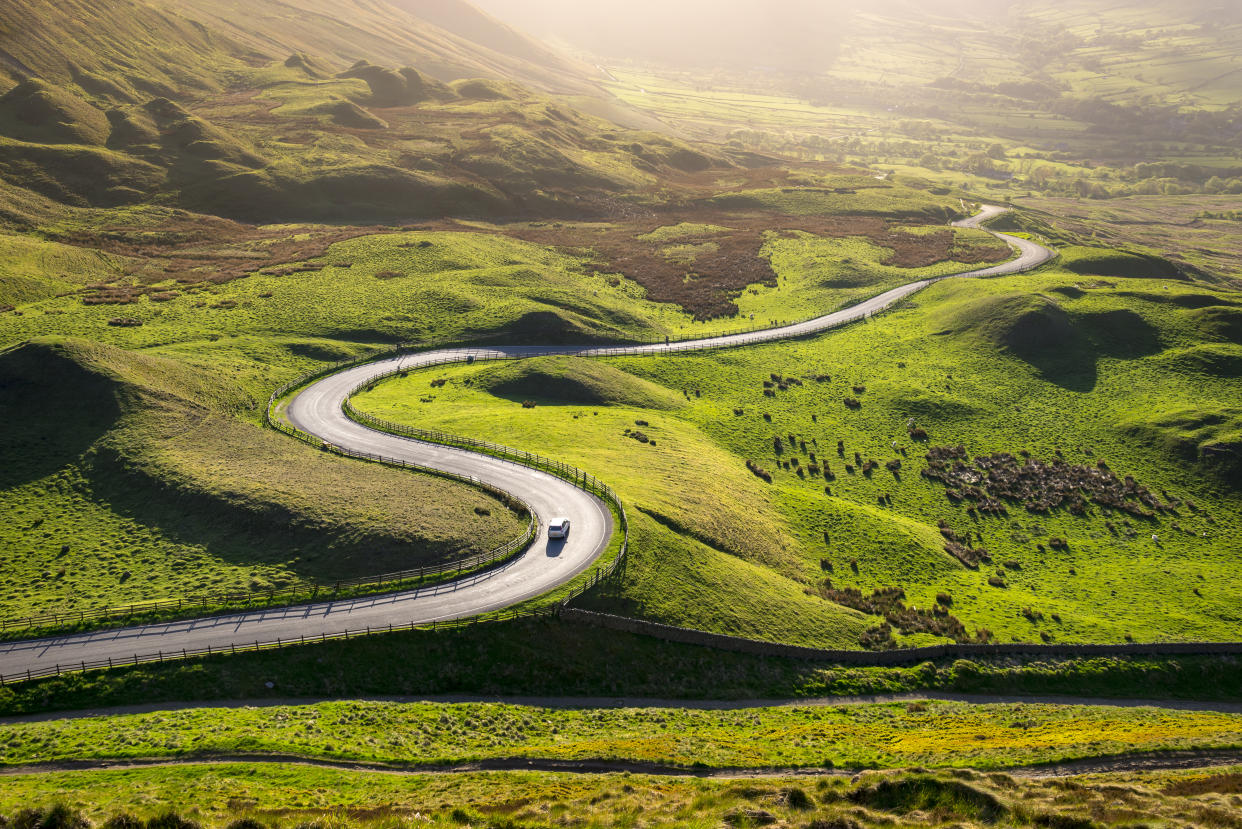 Golden light on the hills of the Peak District, Derbyshire, England. A bendy road leading down into the Edale Valley in early summer.