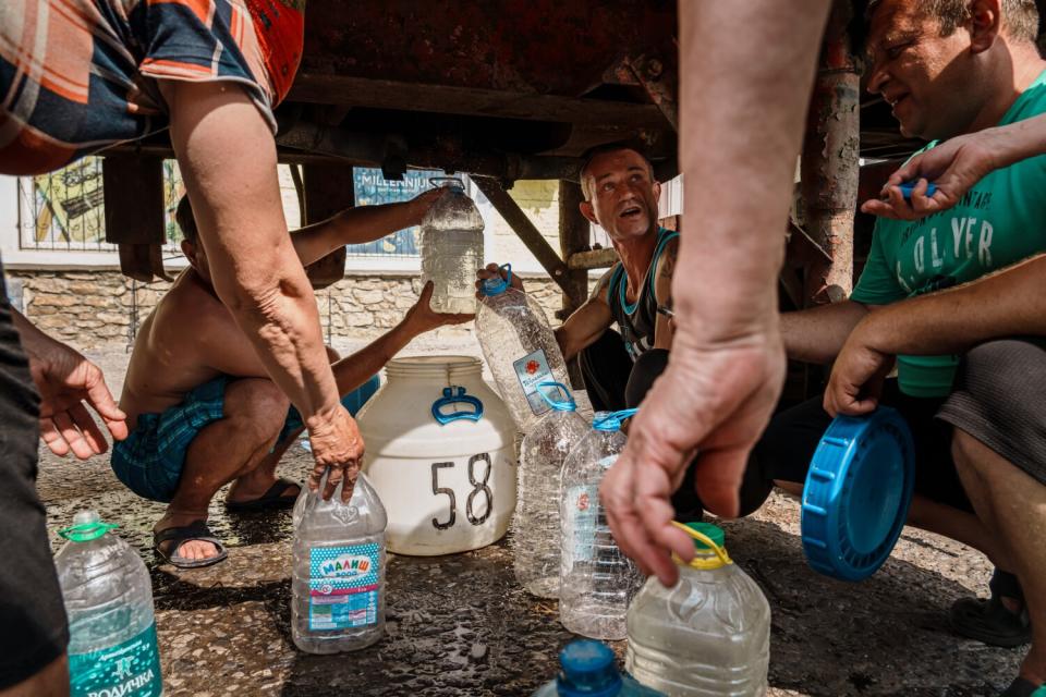 Residents go under the belly of a water truck to collect water in Siversk, Ukraine.