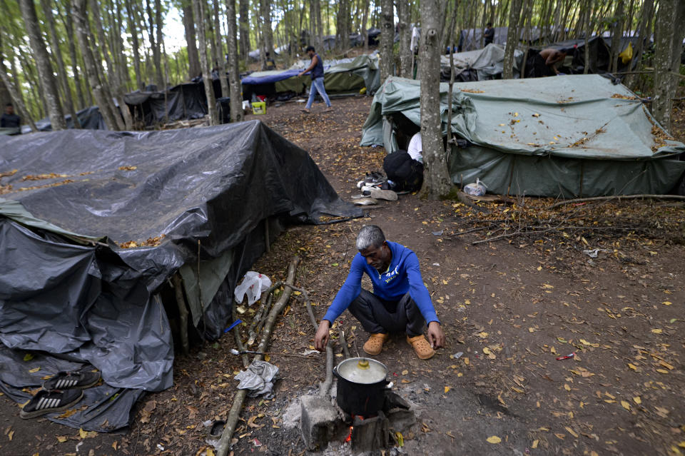 A migrant cooks on an open fire at a makeshift camp in a forest outside Velika Kladusa, Bosnia, Friday, Sept. 25, 2020. (AP Photo/Kemal Softic)