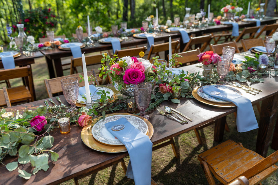 Outdoor wedding place settings for bride and groom at picnic table. Rustic farmhouse flair with roses and vintage mismatched plates.