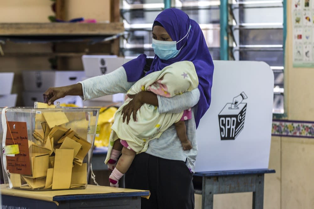 A voter cradles her child as he casts her vote at SK Pulau Gaya September 26, 2020. — Picture by Firdaus Latif