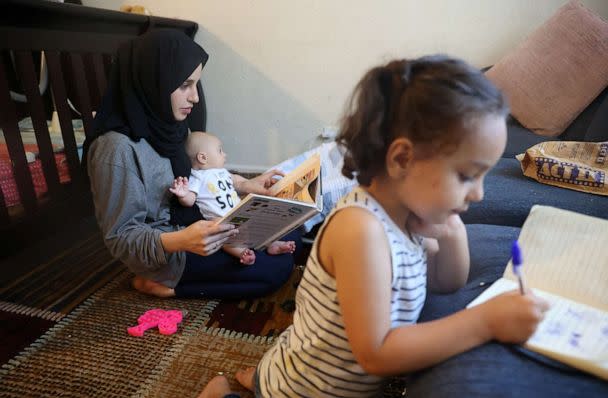 PHOTO: Susan Mohammadi looks over a Dari to English picture book to practice her English while she takes care of her two-month-old son, Yusuf Mohammadi, and daughter Zahra, 3, at their home in Sacramento, Calif., July 12, 2022. (Brittany Hosea-Small/Reuters)
