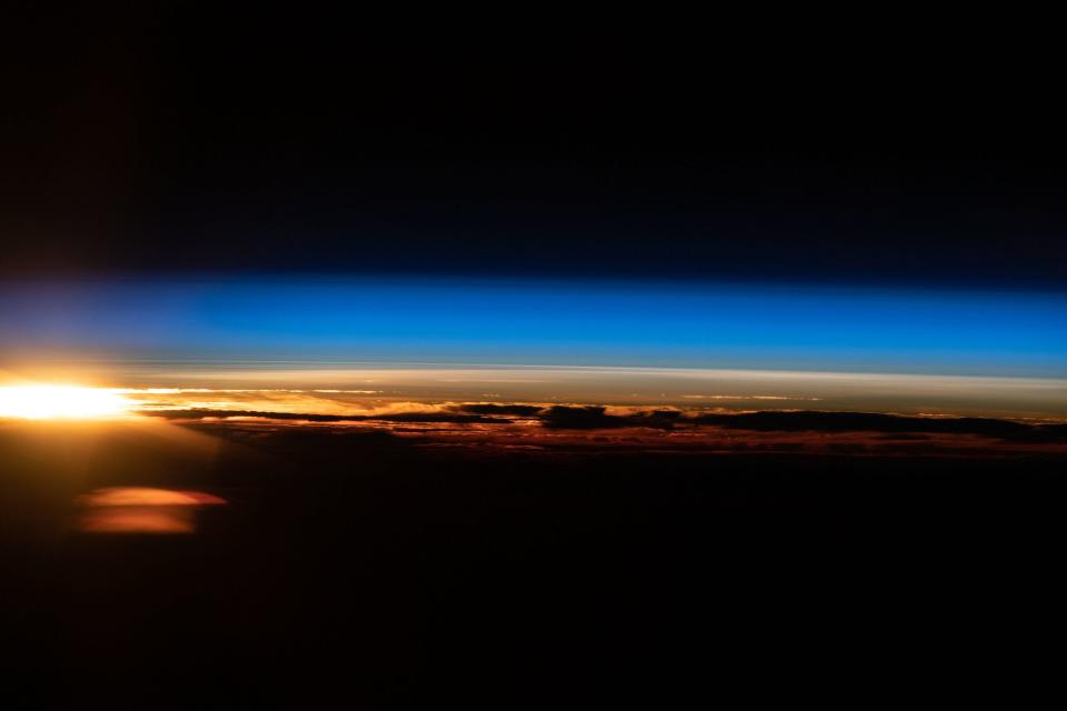 sun rises yellow orange above the dark surface of the earth below blue atmosphere and black space above