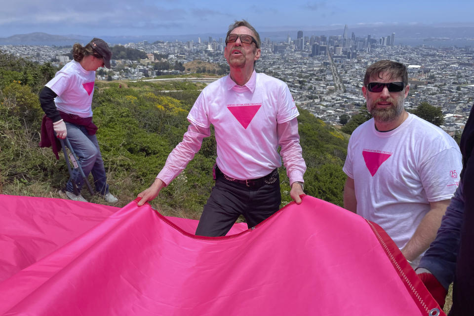 Patrick Carney, center, Co-Founder of Friends of the Pink Triangle, works with volunteers laying out pink tarps to form the shape of a pink triangle on Twin Peaks in San Francisco, Friday, June 16, 2023. Hundreds of volunteers installed the giant pink triangle made out of cloth and canvas and with pink lights around its edges last week as part of the city's Pride celebrations. It's an annual tradition that started in 1995 but this year's triangle is nearly an acre in size and can be seen up to 20 miles (32 kms.) away. (AP Photo/Haven Daley)