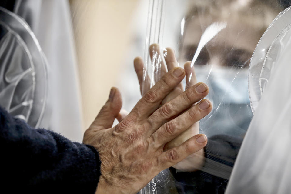 Relatives touch each other's hand through a plastic film screen and a glass to avoid contracting COVID-19 at the San Raffaele center in Rome, Tuesday, Dec. 22, 2020. Italians are easing into a holiday season full of restrictions, and already are barred from traveling to other regions except for valid reasons like work or health. Starting Christmas eve, travel beyond city or town borders also will be blocked, with some allowance for very limited personal visits in the same region. (Cecilia Fabiano/LaPresse via AP)