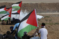 Protesters take cover while waving their national flags from teargas fired by Israeli troops near the fence of Gaza Strip border with Israel during a protest east of Gaza City, Friday, Nov. 16, 2018. (AP Photo/Adel Hana)