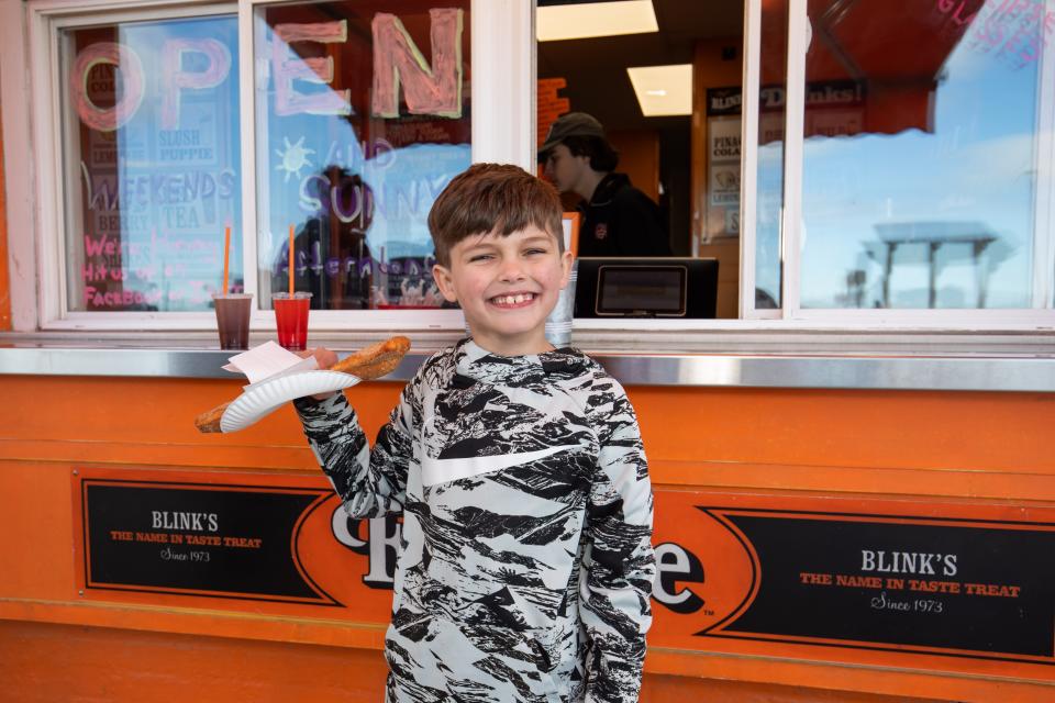 Hampton Beach second-grader Levi Shanahan beams with joy as he savors a freshly made cinnamon and sugar fried dough Sunday, April 7, 2024. Celebrating half a century of sweet memories, Blink’s Fry Doe marks its 50th anniversary.