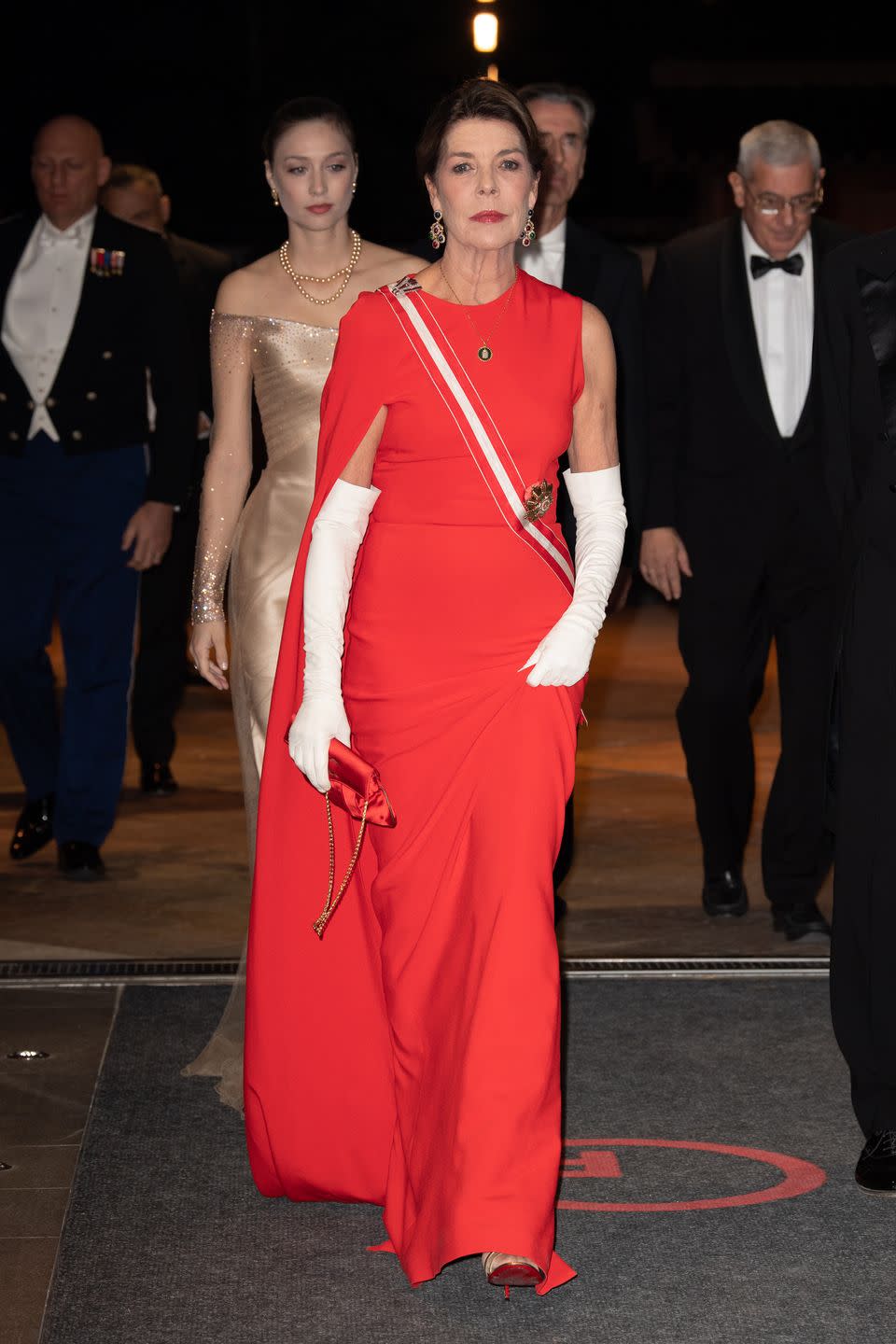 <p>The Monaco royal wore the same asymmetrical Stella McCartney cape dress for 2018's Monaco National Day gala. Princess Caroline paired the gown with long white gloves and a red satin purse. <br></p>