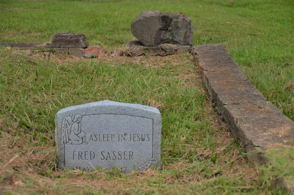 A partially sunken headstone bears the image of an angel beside the inscription "Asleep in Jesus."