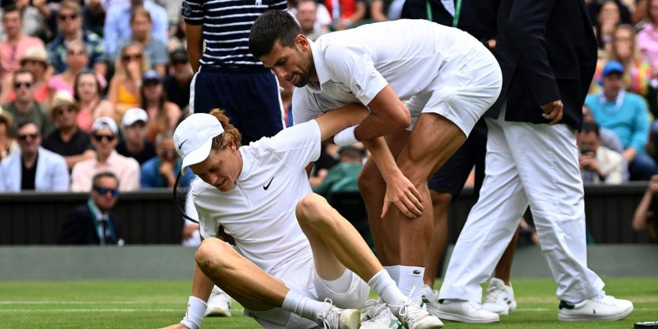 Novak Djokovic helps Jannik Sinner to his feet at Wimbledon.