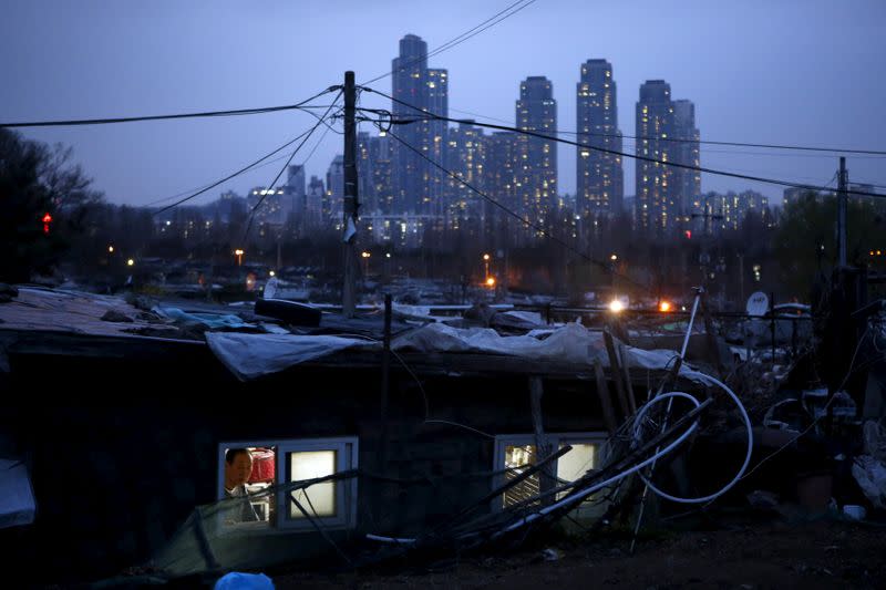 FILE PHOTO: A man looks out from his shack as a luxury high-rise apartment complex is seen in the background at Guryong village in Seoul