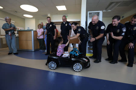 Dr. Daniela Carvalho (L) controls remotely as Andrea Destraio, 5, slaps hands with police officers who donated money to Rady Children's Hospital, as they unveil a program that uses remote control cars to take young patients to the operating room, in San Diego, California, U.S. September 19, 2017. REUTERS/Mike Blake