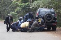 Police officers and members of the media take cover at a distance from the Westgate Shopping Centre after continuous gunfire was heard coming from the mall in Nairobi September 23, 2013. REUTERS/Siegfried Modola