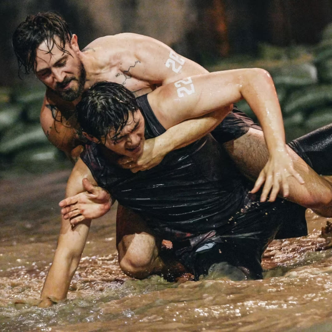  Two men (justin harvey and another contestant) wrestle in a pit of shallow water, in 'physical 100' season 2. 