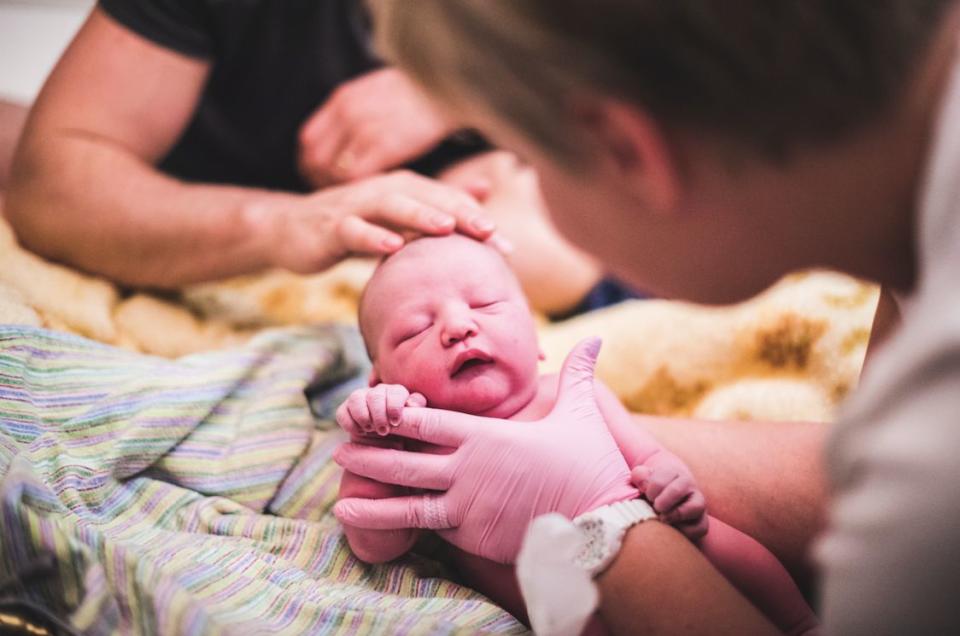 "This midwife is doing a newborn check-up of a little baby boy. She was so gentle with him that he slept throughout the examination, and because this was a home birth, the check up was done on mom and dad's bed. You can see dad gently stroking baby's head." ​