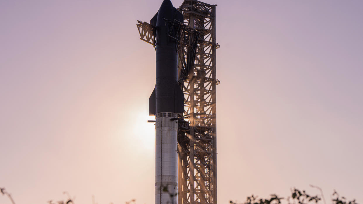  Spacex's huge starship vehicle stands next to its launch tower, blocking out the sun in the background. 