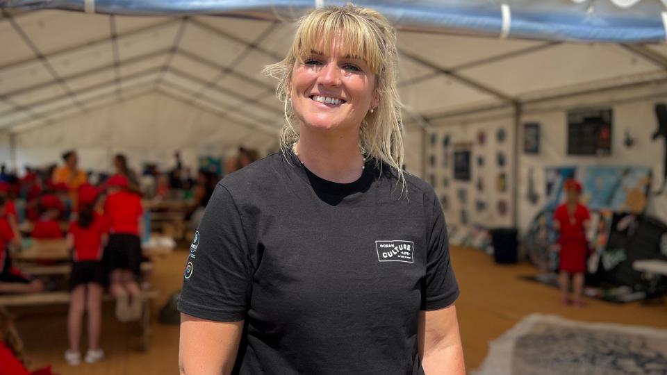 Tamsin smiles at the camera as children learn inside a big tent behind her