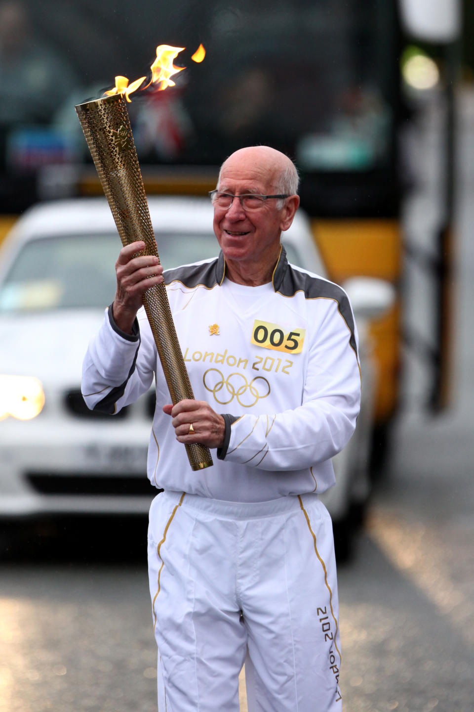 In this handout image provided by LOCOG, Torchbearer 005 Sir Bobby Charlton carries the Olympic Flame on the Torch Relay leg between Salford and Moss Side on Day 37 of the London 2012 Olympic Torch Relay on June 24, 2012 in Manchester, England. The Olympic Flame is now on day 37 of a 70-day relay involving 8,000 torchbearers covering 8,000 miles. (Photo by LOCOG via Getty Images)