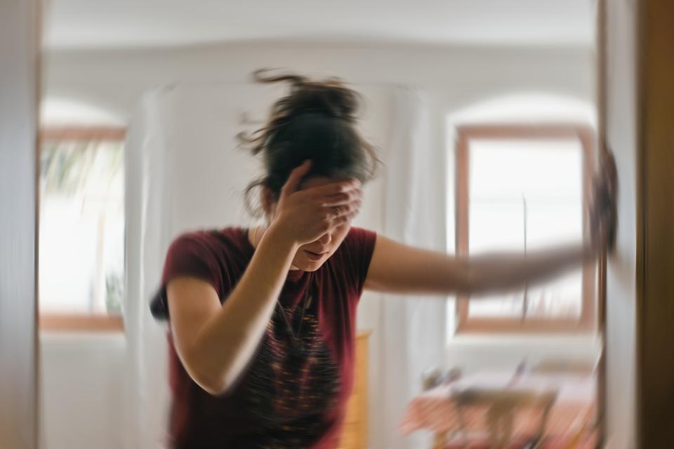 A woman holds one hand to her head and steadies herself against a door frame as the room behind her appears to spin as she suffers from vertigo