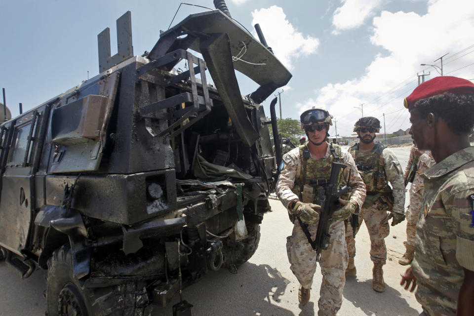 Two members of the Italian military and a Somali soldier, right, walk next to a damaged armored personnel carrier after an attack on a European Union military convoy in the capital Mogadishu, Somalia Monday, Oct. 1, 2018. A Somali police officer says a suicide car bomber has targeted a European Union military convoy carrying Italian military trainers in the Somali capital Monday. (AP Photo/Farah Abdi Warsameh)