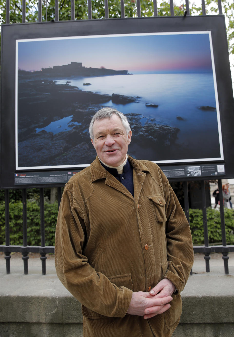 British photographer Michael St Maur Sheil poses in front of one of his pictures displayed at the Paris Luxembourg gardens, Tuesday, April 8, 2014, as part of an exhibition " Fields of Battle - Lands of Peace 14-18 ". The picture displayed is a modern take at the location of the Cape Helles landings on the Gallipoli peninsula. Captured over a period of seven years, Michael’s photography combines a passion for history and landscape and presents a unique reflection on the transformation of the battlefields of the Great War into the landscape of modern Europe. (AP Photo/Christophe Ena)