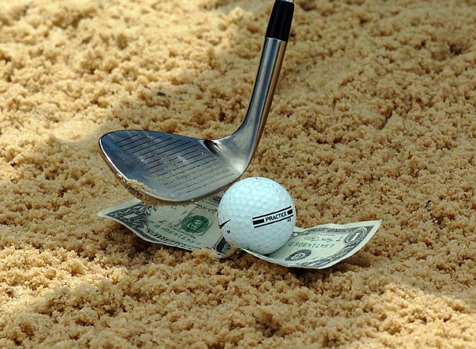 In this 2006 photo, golf pro Dana Rader shows how to use a dollar bill to hit a bunker shot. Rader taught golfers to place the ball in the center of the dollar. The entire bill would land onto the green with a good shot. A dig or chop at the ball would cut the dollar in half, and hitting too far behind the dollar would leave the ball in the bunker.