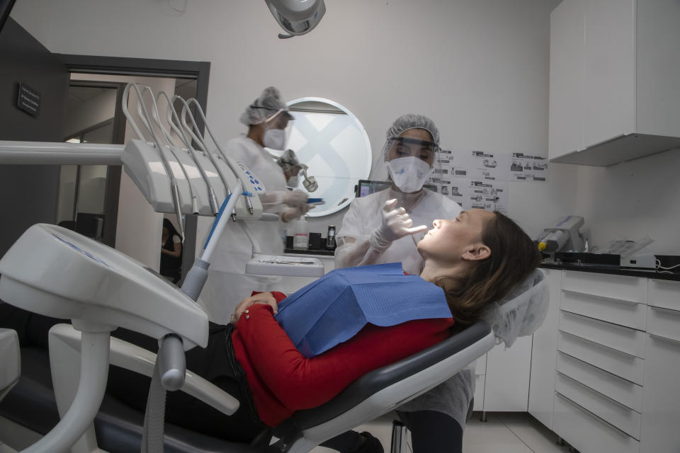 In this Wednesday, May 13, 2020 photo, dentist Sabrine Jendoubi, speaks to patient Veronique Guillot during a dental appointment, at a dental office in Paris. Those with toothache that suffered through France's two-month lockdown, finally have hope to end the pain. Dental practices are cautiously re-opening and non-emergency dentist appointments are now permitted around the country, as the French government eased confinement restrictions from Monday. (AP Photo/Michel Euler)