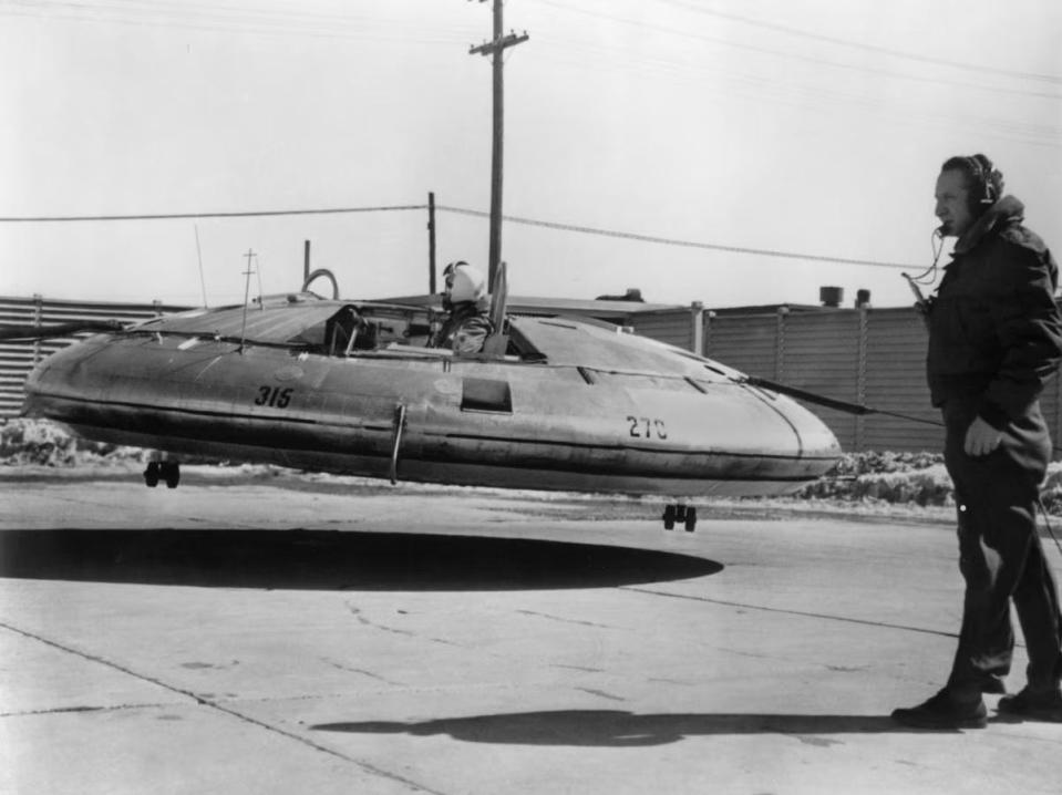 An image of the Avrocar hovering above the ground while a pilot operates the ship while being watched by another man.