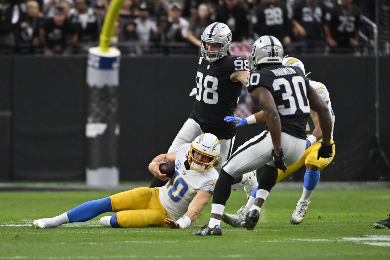 Justin Herbert (10) slides before Raiders Maxx Crosby (98) and Duron Harmon (30) can hit the Chargers' quarterback.