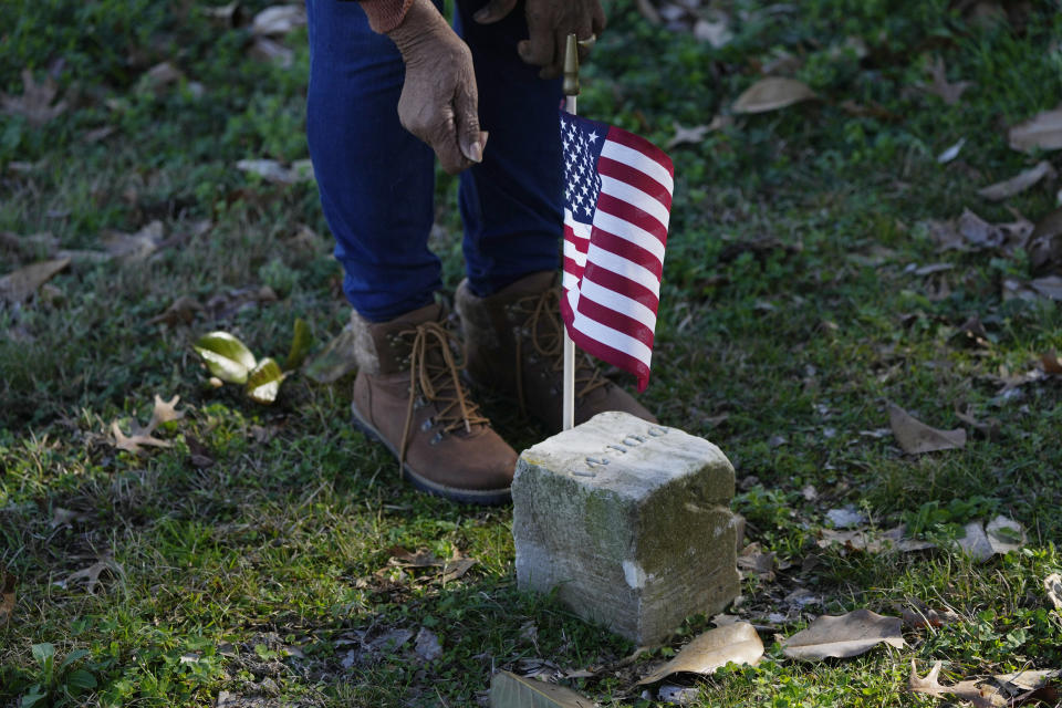 Thelma Sims Dukes places an American flag by the grave of a Civil War soldier of the United States 1st Mississippi Infantry (African Descent) in Vicksburg National Cemetery, Feb. 14, 2024, in Vicksburg, Miss. Thirteen flags were placed at the graves of the Black soldiers killed in an 1864 massacre at Ross Landing, Arkansas, who were buried as unknowns but have recently been identified. As a child, Dukes walked to school across the grounds of Vicksburg National Military Park. (AP Photo/Rogelio V. Solis)