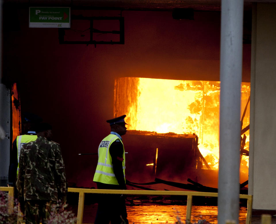 Policemen look at the fire near the international arrivals unit of Jomo Kenyatta International Airport, Nairobi, Kenya, Wednesday, Aug. 7, 2013. A massive fire engulfed the arrivals hall at Kenya's main international airport early Wednesday, forcing East Africa's largest airport to close and the rerouting of all inbound flights. Dark black smoke that billowed skyward was visible across much of Nairobi as emergency teams battled the blaze. (AP Photo/Sayyid Azim)