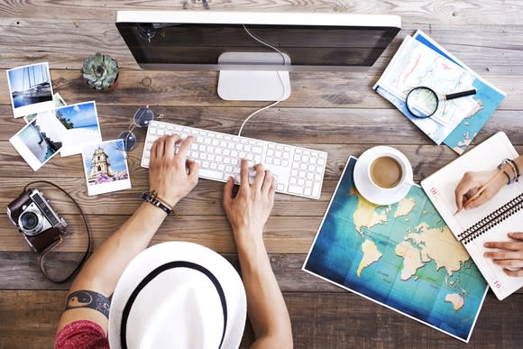 Overhead view of a young couple planning a vacation at their computer with maps and pictures on a desk