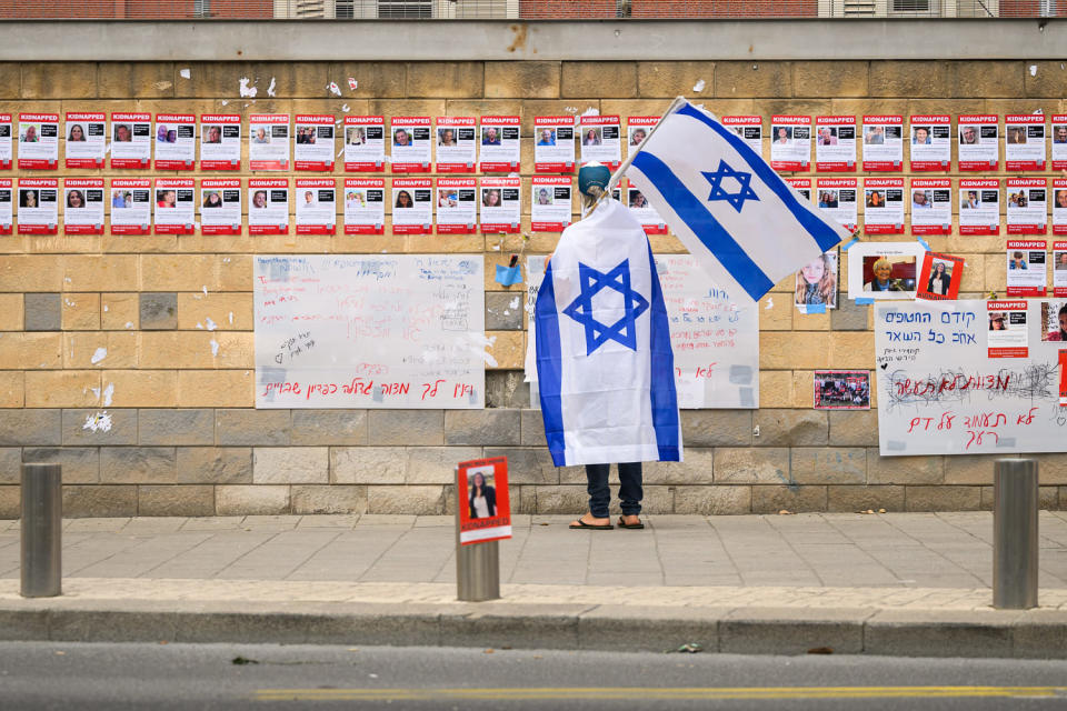 A person wrapped in an Israeli flag looks at photographs of some of those taken hostage by Hamas  in Tel Aviv on Oct. 18, 2023. (Leon Neal / Getty Images)