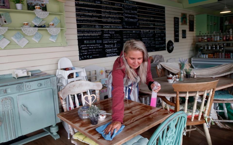 A woman cleans a table in cafe - Darren Staples/Getty Images