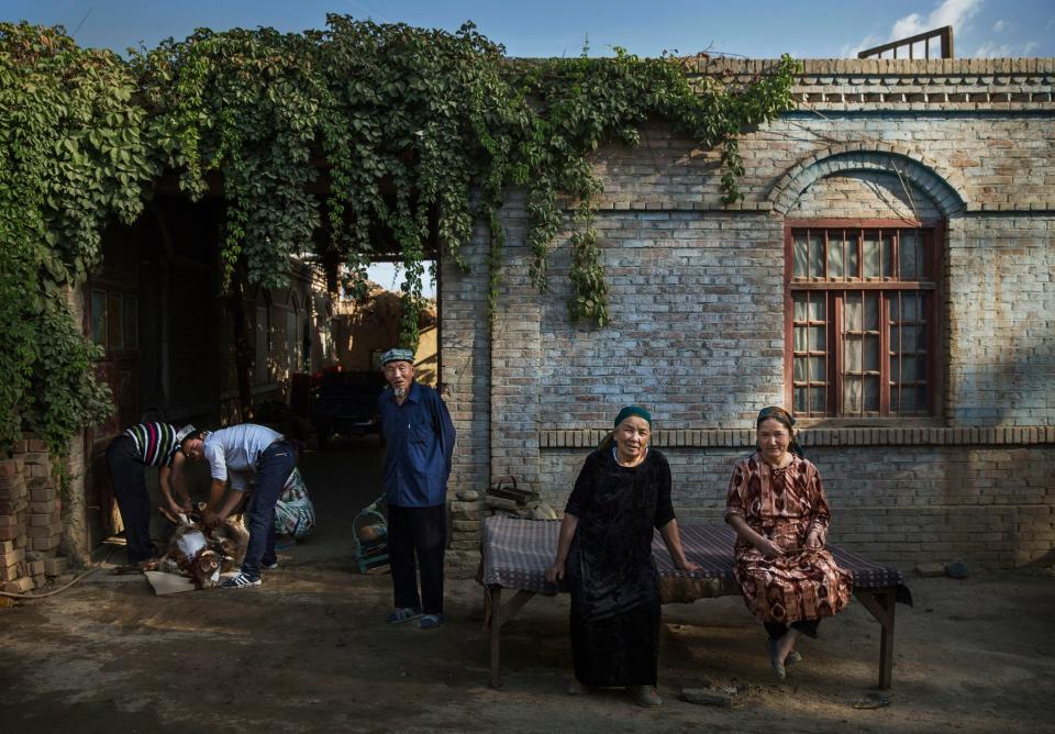 Uyghur women sits in front of their house as her family slaughters a goat, left, on the morning of the Corban Festival in Turpan County, in the far western Xinjiang province, China