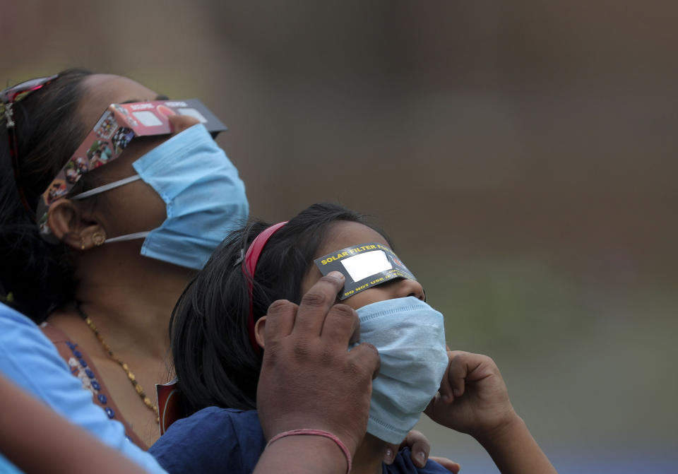 Indians wearing masks as a precaution against coronavirus watch solar eclipse through solar filters in Hyderabad, India, Sunday, June 21, 2020. (AP Photo/Mahesh Kumar A.)