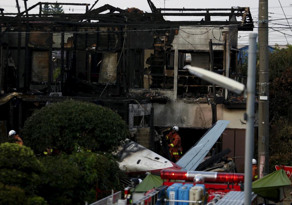 Firefighters remove wreckage and debris at the site where a light plane went down in a residential area and burst into flames, in Chofu