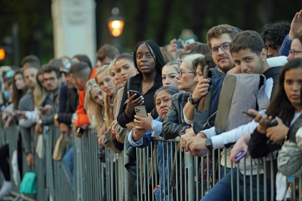 A crowd of people leans on steel barriers at Buckingham Palace after the death of Queen Elizabeth II.