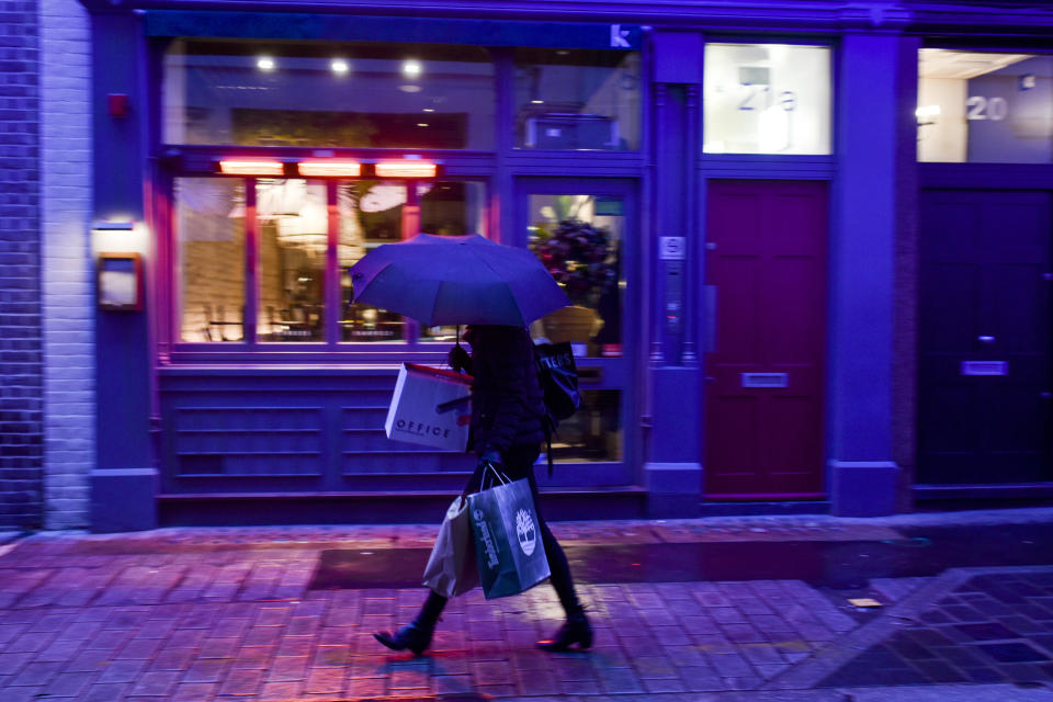 A woman wears a face mask as she carries shopping bags in Soho, in London, Wednesday, Dec. 16, 2020. London and some of its surrounding areas will be placed under Britain's highest level of coronavirus restrictions beginning at 00:01 local time on today as infections rise rapidly in the capital. Under Tier 3 restrictions, the toughest level in England's three-tier system, people can't socialize indoors, and bars, pubs and restaurants must close except for takeout.(AP Photo/Alberto Pezzali)