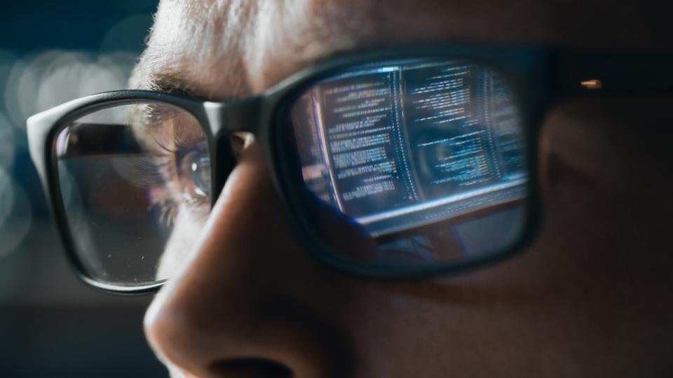  A man wearing glasses with computer code reflected in the glass 