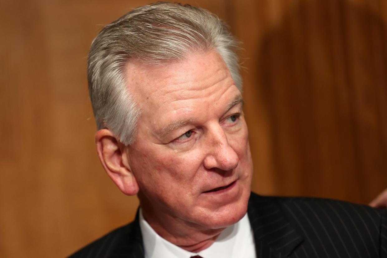 A close-up of Tommy Tuberville against a wood-paneled wall, wearing a pinstripe suit, white shirt and red tie.