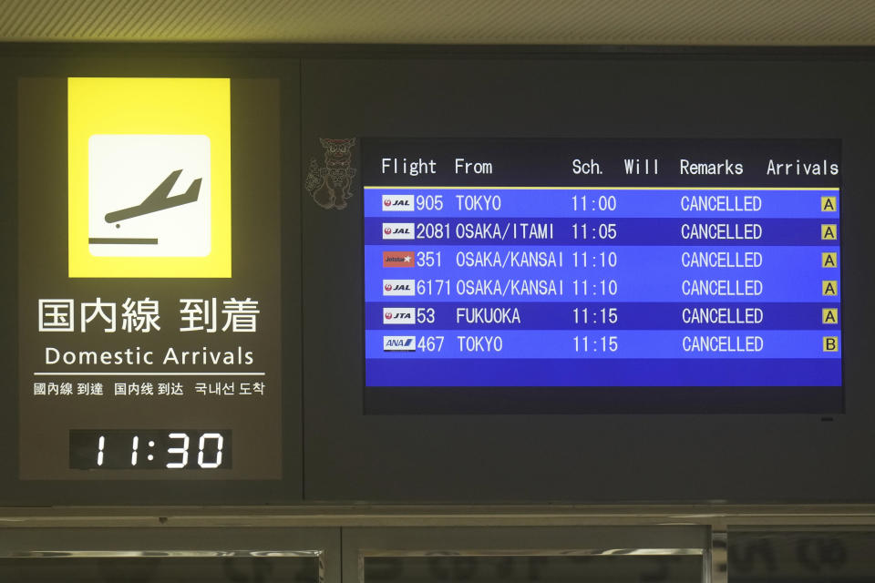 Electric boards show some of the domestic arrival flights to Naha Airport are canceled at its lobby, seen through the door of an airport entrance, in Naha in the main Okinawa island, southern Japan, Thursday, June 1, 2023. A tropical storm headed toward Japan's southern archipelago of Okinawa on Thursday, leading businesses and the airport to close and fishermen to batten down their boats in preparation. (AP Photo/Hiro Komae)