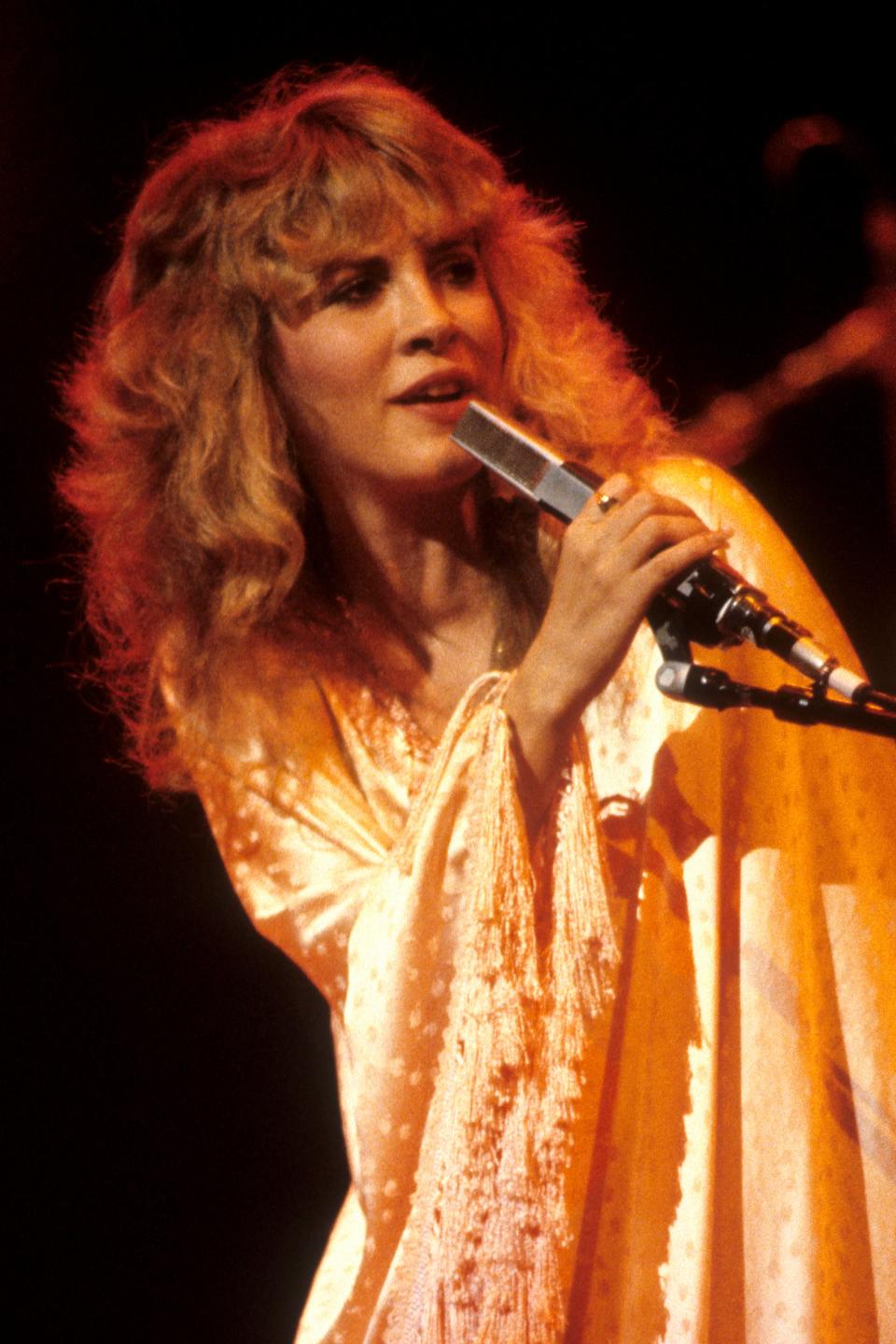 Stevie Nicks on stage singing into a microphone, wearing a flowing shawl