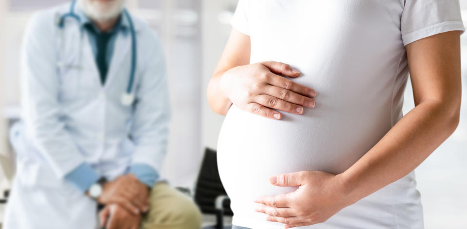 A pregnant woman holds her stomach as a doctor sits behind her