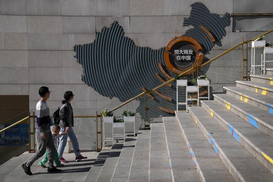 A family walks by a map showing Evergrande development projects in China at an Evergrande city plaza in Beijing, Tuesday, Sept. 21, 2021. Global investors are watching nervously as the Evergrande Group, one of China's biggest real estate developers, struggles to avoid defaulting on tens of billions of dollars of debt, fueling fears of possible wider shock waves for the Chinese financial system. (AP Photo/Andy Wong)